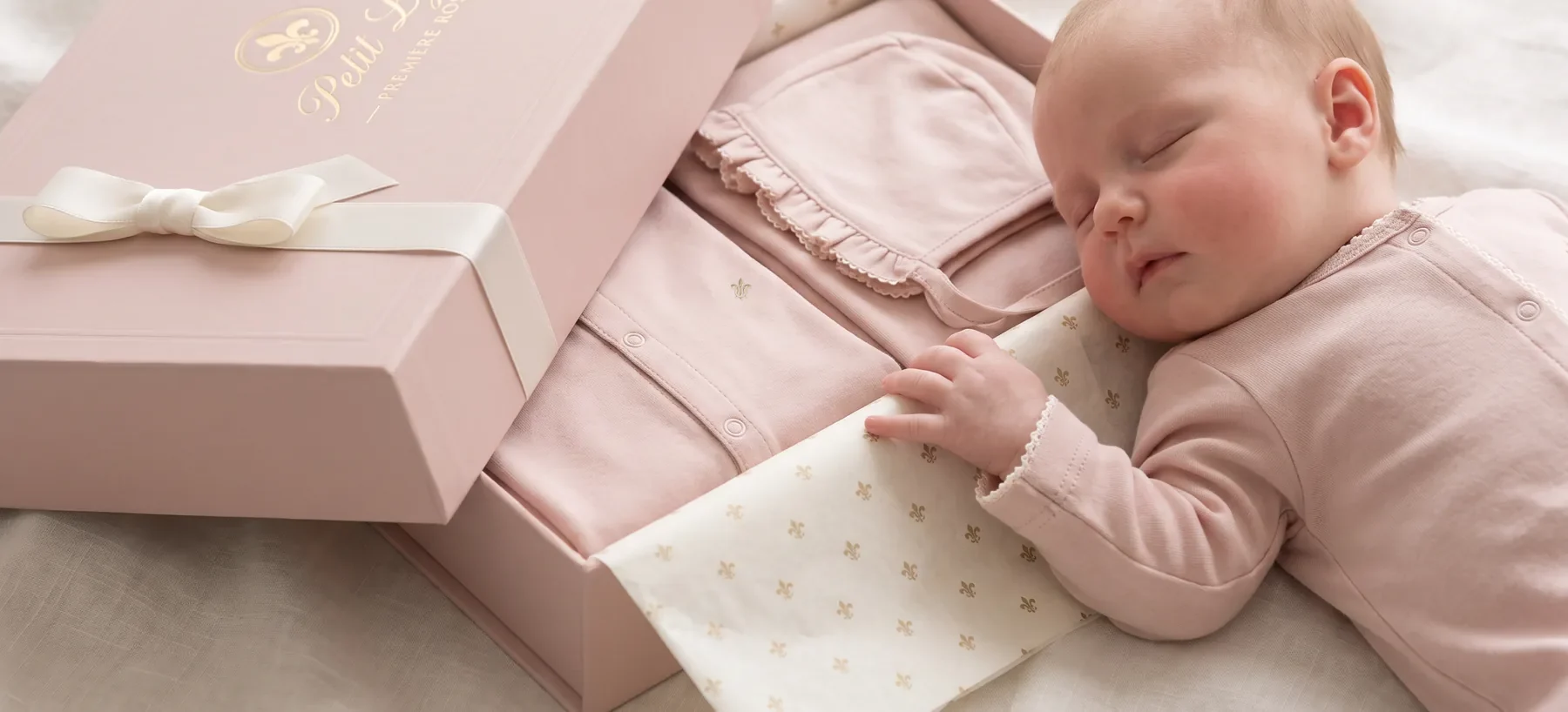 The Première Rose gift box opened in lily tissue, a newborn asleep beside it